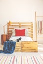 Vertical view of comfortable bed with wooden headboard, red pillow and bright bedding, bedroom interior with copy space on the whi