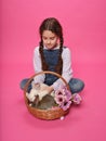 Cute schoolgirl plays with two bunnies, puts them in a basket, poses in the studio, on a pink background. Royalty Free Stock Photo