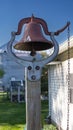 Vertical view of a farm dinner bell on the outdoors with a garden and blue sky in the background Royalty Free Stock Photo