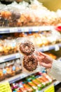 Vertical view of female hand showing to camera brown chocolate frosting with sprinkle doughnut in a supermarket while grocery Royalty Free Stock Photo