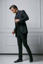 Full length picture of an elegant young fashion man adjusting his suit while looking to his side, on white background. Royalty Free Stock Photo