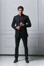 Vertical view. Full length picture of an elegant young man adjusting his suit while looking to his side, looking at camera, on Royalty Free Stock Photo