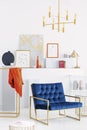 Golden chandelier above petrol blue settee in white modern art collector`s apartment, real photo