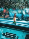 Vertical view of a Hula Girl figurine on the dashboard of a classic American car on a rainy day