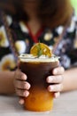 Vertical view, Iced coffee mixed with orange juice in a tall glass with a woman hand.
