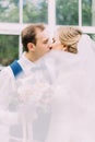 Vertical view of the kissing newlyweds behind the overblowing veil. Royalty Free Stock Photo