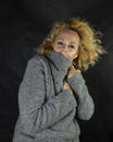 Middle-aged blonde woman shelters from the cold and wind with a wool jacket, closing it up to her face