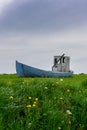 Vertical view of an old abandoned wooden fishing boat in a green grassy meadow with flowers in the foreground