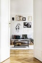Vertical view of open door to living room interior with grey sofa, industrial coffee table and golden chandelier Royalty Free Stock Photo