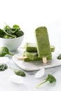 Vertical view of a stack of green smoothie popsicles with one standing in front and a bowl of spinach in behind.