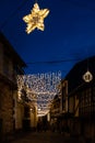 Vertical view of a street illuminated at Christmas with a star and lights, background with people walking between the stone houses Royalty Free Stock Photo