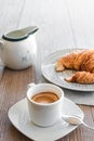 Vertical view of a white cup of espresso coffee with a small saucer with milk and a croissant on a dish on the background on the Royalty Free Stock Photo