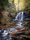 Vertical of a waterfall cascading down the rocks in a forest in autumn Royalty Free Stock Photo