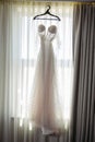 Vertical of a wedding dress on a hanger against a window Royalty Free Stock Photo