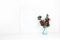 Vertical white blank wooden frame mockup. Holly berry branches in blue glass vase on white table. Styled stock feminine