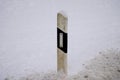 Vertical of a white painted concrete road bollard in the snowy ground