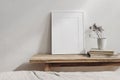 Vertical white picture frame mockup. Vintage wooden bench, table. Cup with dry grass on pile of books. White wall