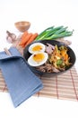 Vertical, wide studio shot of black bowl of ramen noodles with boiled eggs, veggies and turkey meet, ready to be poured