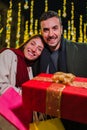 Vertical. young couple smiling and holding a christmas present with a ribbon. Two happy friends giving a surprise