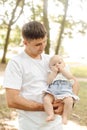 Vertical. Young cute dad carefully holds his newborn daughter in his arms on summer day outside.