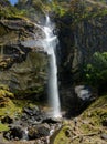 VERTICAL: Young female traveler is walking up to a high waterfall in Tibet.