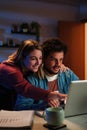 Vertical Young happy caucasian couple browsing on internet using a laptop to search sale at home. Excited husband and