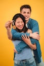 Vertical. Young multiracial homeowner couple holding and showing the key of their new apartment at yellow color backdrop