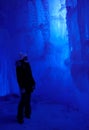 VERTICAL: Young woman exploring an icecave looks at a beautiful ice formation.