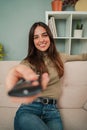 Vertical. young woman using the television remote controller to change the channel. Adult caucasian female turning on