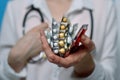 Vertically folded packs with different pills in a woman`s hand and a stethoscope around her neck