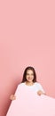 Vertival flyer with young pretty girl in white t-shirt holding huge empty sheet of paper isolated on pink background