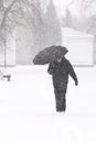 Very bad weather in a city in winter: heavy snowfall and blizzard. Male pedestrian hiding from the snow under umbrella, vertical Royalty Free Stock Photo