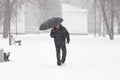 Very bad weather in a city in winter: terrible heavy snowfall and blizzard. Male pedestrian hiding from the snow under umbrella