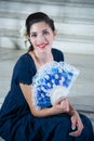 Cute girl, with long blue dress, with fan, sitting on background steps Royalty Free Stock Photo