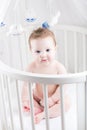 Very beautiful baby sitting in a white round crib