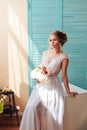 Very beautiful blonde with blue eyes in a white bride dress near a window with a bouquet of flowers Royalty Free Stock Photo