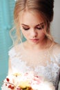 Very beautiful blonde with blue eyes in a white bride dress near a window with a bouquet of flowers Royalty Free Stock Photo