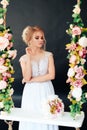 Very beautiful blonde with blue eyes in white dress a bride on a swing in studio on a black background with a bouquet of flowers