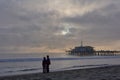 Very beautiful sunset in Santa Monica, a couple on the sand in the foreground, pier to the right, sea buoys and a cloudy sky in Royalty Free Stock Photo