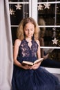 A very beautiful teenage girl in a New Year`s interior of an apartment or house near the window reads a book Royalty Free Stock Photo