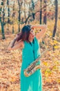 Very beautiful young woman with black hair raised her hands to her head and stands with an alto saxophone in a long blue dress amo Royalty Free Stock Photo