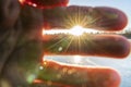 Very bright low winter Sun shines with rays and lens flares between very close, horizontally placed to camera blurry fingers,