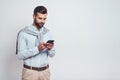 Very busy. Handsome young man in casual wear using his smart phone while standing on a grey background. Digital concept