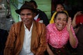 very cheerful laughing and fumbling Indonesian elderly woman in a pink blouse and her stylishly dressed man in a brown hat