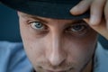 Very close portrait of a young blue-eyed man who with his hand adjusts the black hat on his head Royalty Free Stock Photo