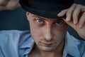 Very close portrait of a young blue-eyed man who with his hand adjusts the black hat on his head Royalty Free Stock Photo