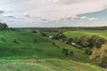 Colorful Bright Summer Sunny Green Field Landscape With Blue Cloudy Sky, River Trees And Hills