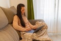 Very concentrated and serious woman sitting on a sofa and covered with a blanket works on her laptop from home