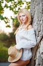 Very cute blond woman sitting down outdoor with a hat near a tree Royalty Free Stock Photo