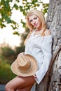 Very cute blond woman sitting down outdoor with a hat near a tree Royalty Free Stock Photo